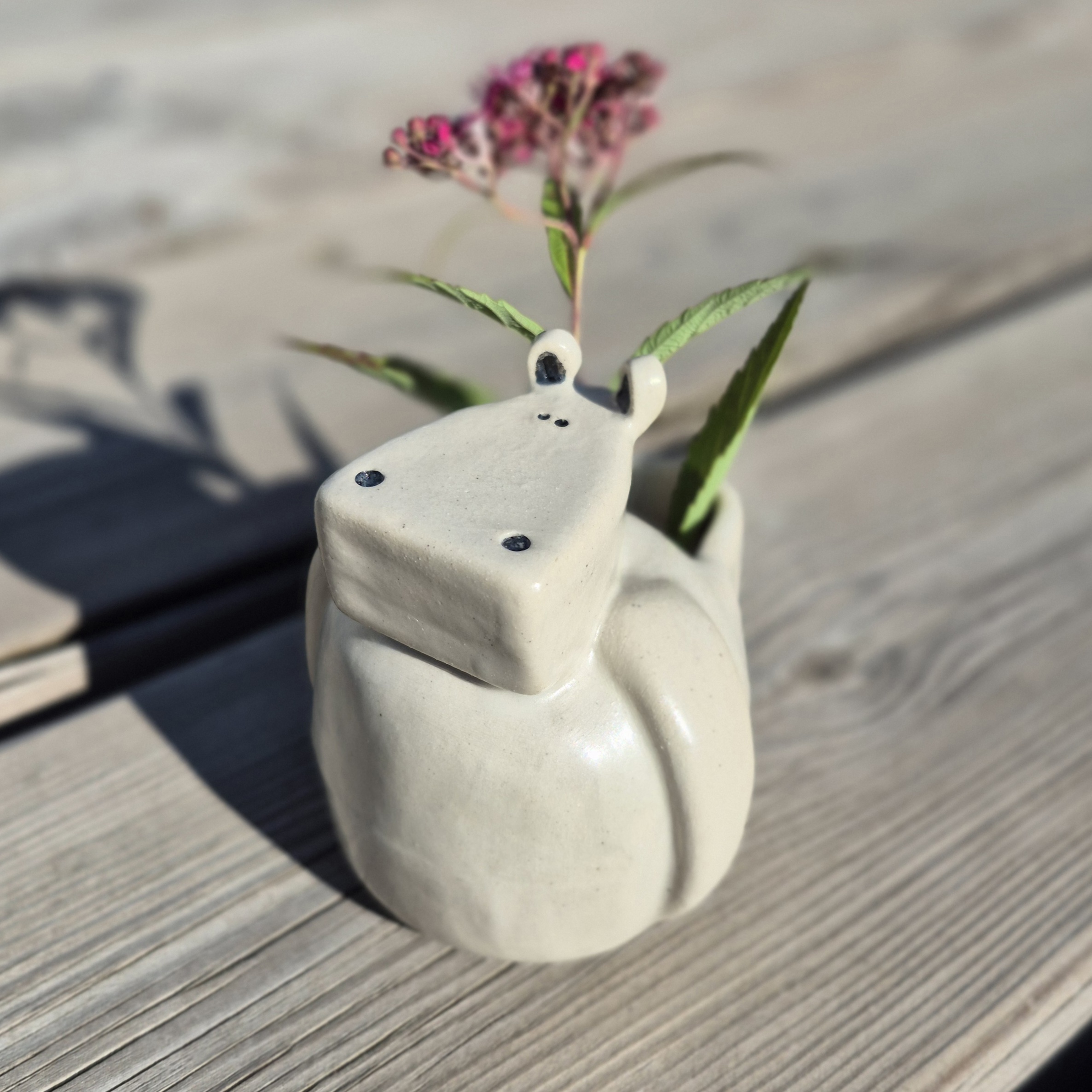 Petit vase hippopotame en céramique artisanale avec fleurs sur une table en bois au soleil