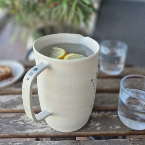 Pichet Géometrik en grès fait main avec décor graphique peint aux engobes, photographié sur une table en bois avec eau citronnée